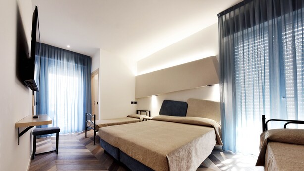 A hotel room with two beds, a desk, a chair, and a TV mounted on the wall.