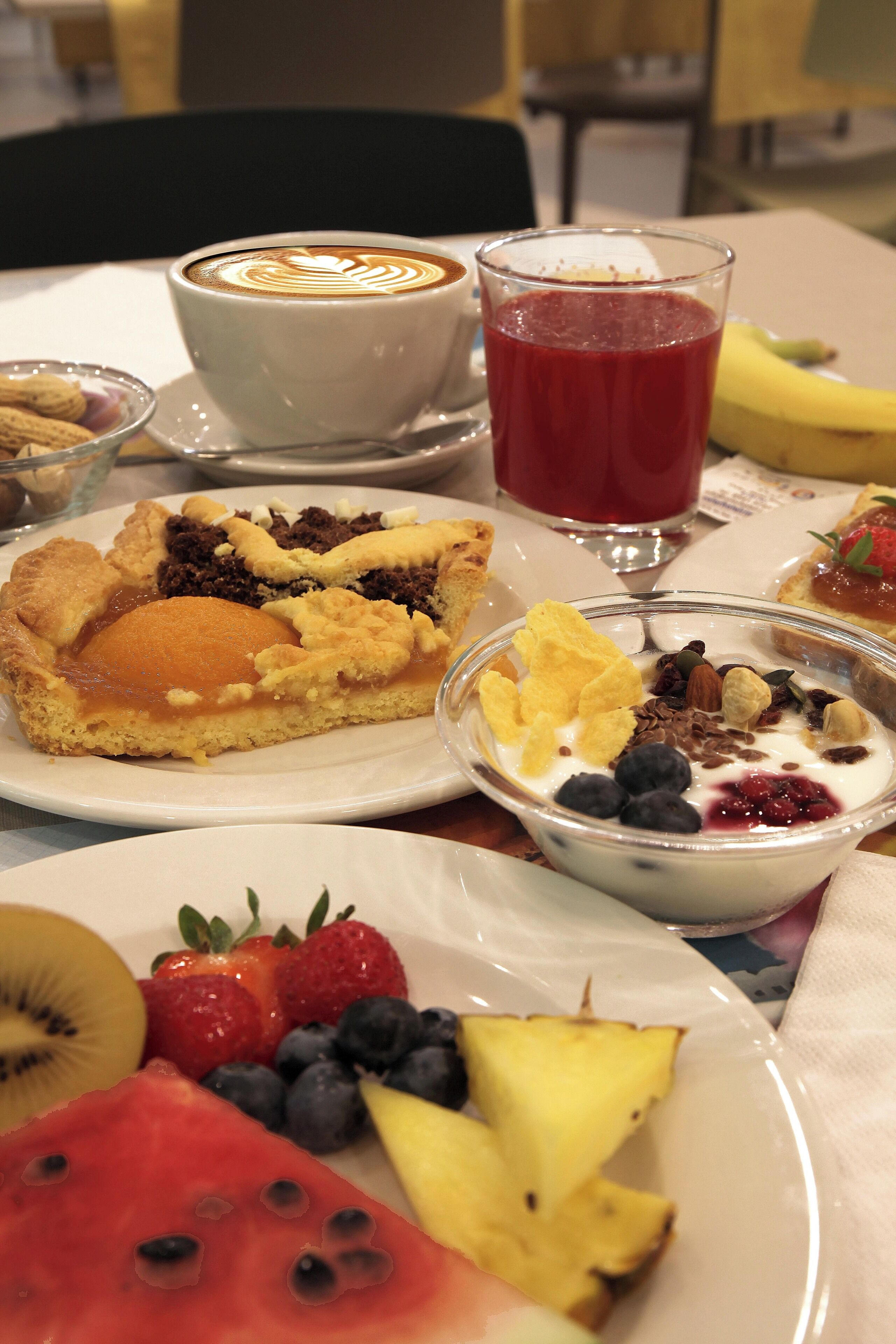 A table with a variety of food items including a pie, a glass of red juice, and a bowl of yogurt with fruits.