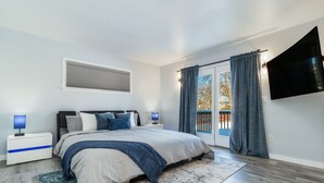 Een slaapkamer met een bed, nachtkastjes, een televisie en een balkon met gordijnen.