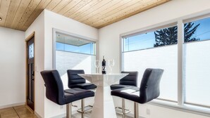 Een moderne eetruimte met een witte tafel en vier zwarte stoelen, twee wijnglazen en een fles op tafel.