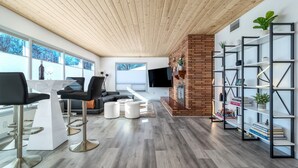 Een moderne woonkamer met een houten plafond, een bakstenen open haard en een boekenkast.