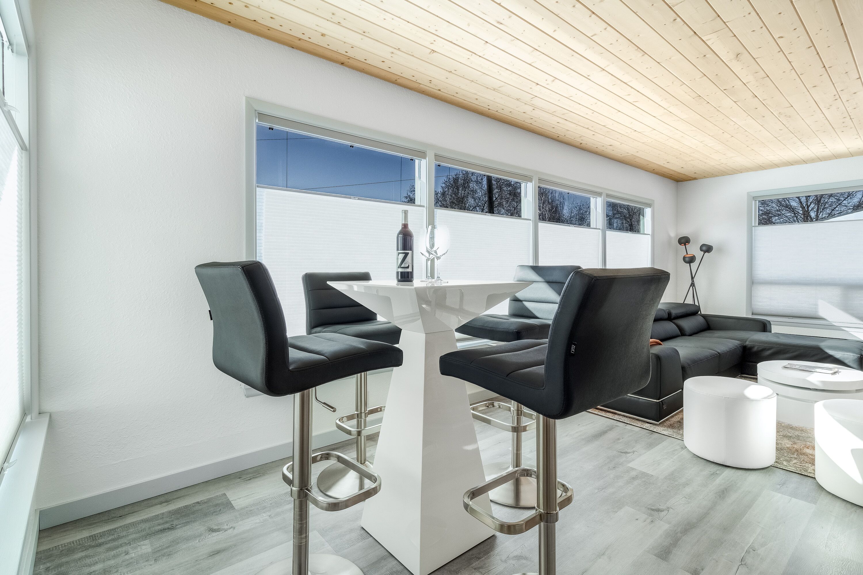 Un salon moderne avec une table basse blanche, un canapé en cuir noir et deux tabourets de bar noirs.