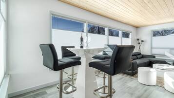Un salon moderne avec une table basse blanche, un canapé en cuir noir et deux tabourets de bar noirs.