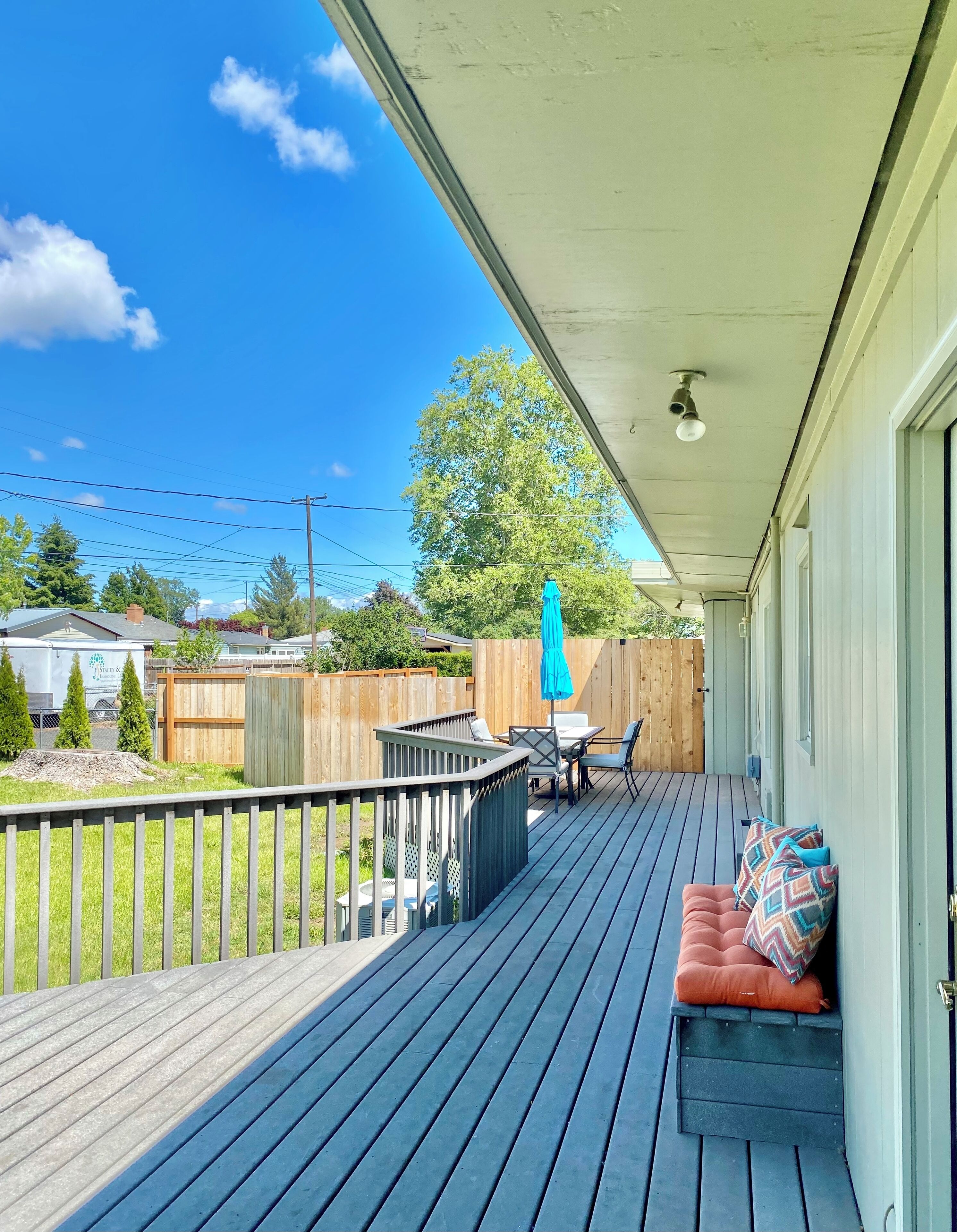 A covered deck with a blue railing, outdoor furniture, and a view of the backyard.