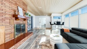Een moderne woonkamer met een bakstenen open haard, een zwarte leren bank en een houten plafond.