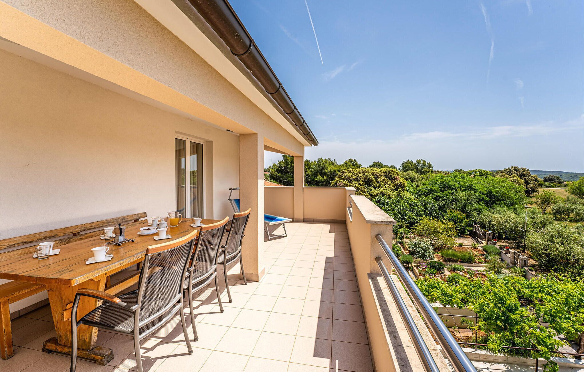 Ein Balkon mit Holztisch und Stühlen, Blick auf Grün und einen klaren Himmel.