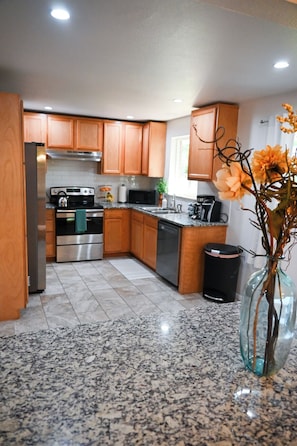 A modern kitchen with wooden cabinets, stainless steel appliances, granite countertops, and a vase with flowers.
