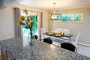 A dining area with a granite countertop, white chairs, a table set with plates and flowers, and a hanging light fixture. - Spacious, Quiet Home in Centennial (Centennial)
