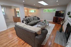 A living room with a sofa, coffee table, TV, fireplace, and a dining area in the background.