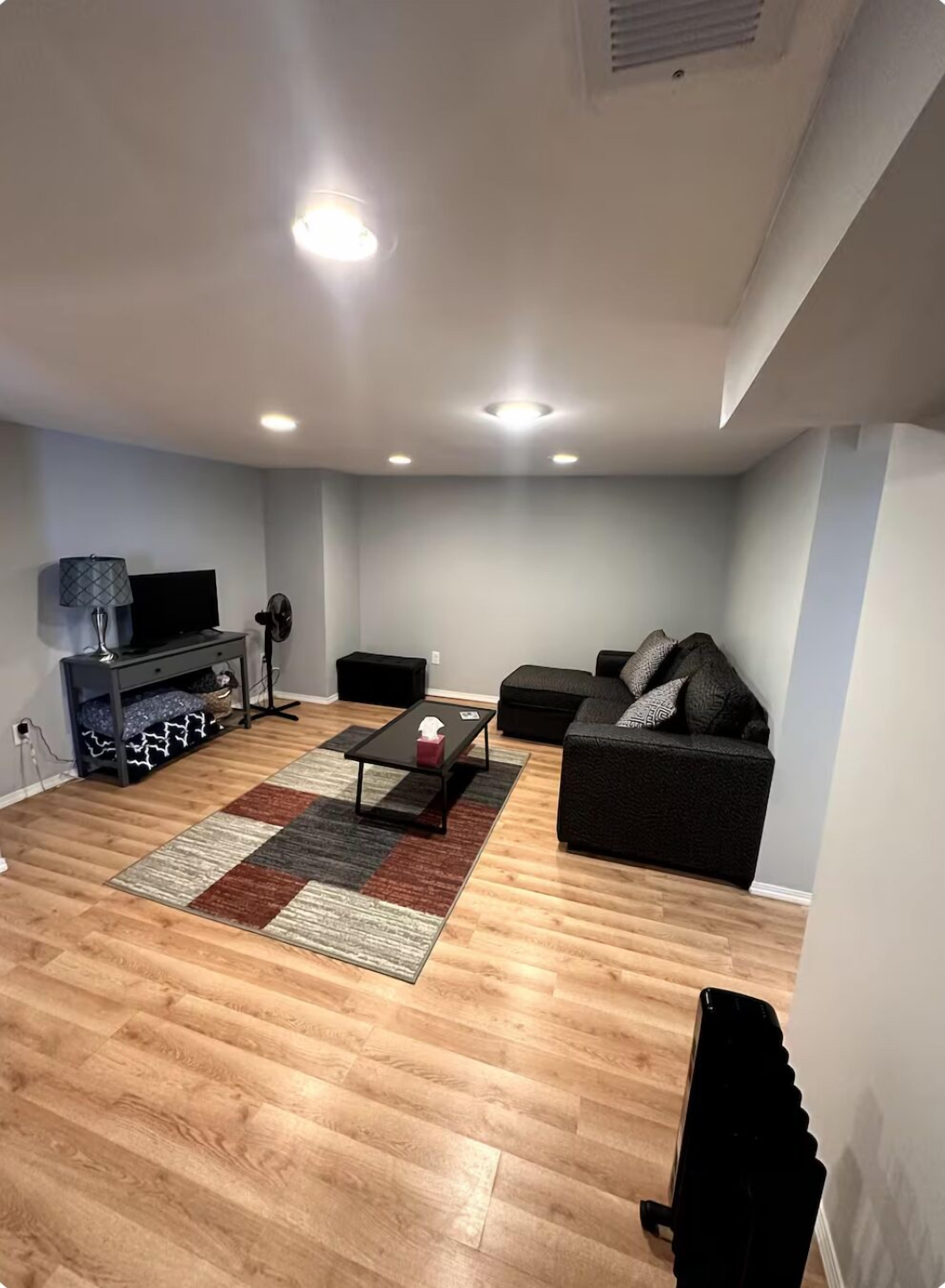 Ein modernes Wohnzimmer mit Holzboden, einer schwarzen Couch, einem Couchtisch und einem Fernseher auf einem Standfuß.