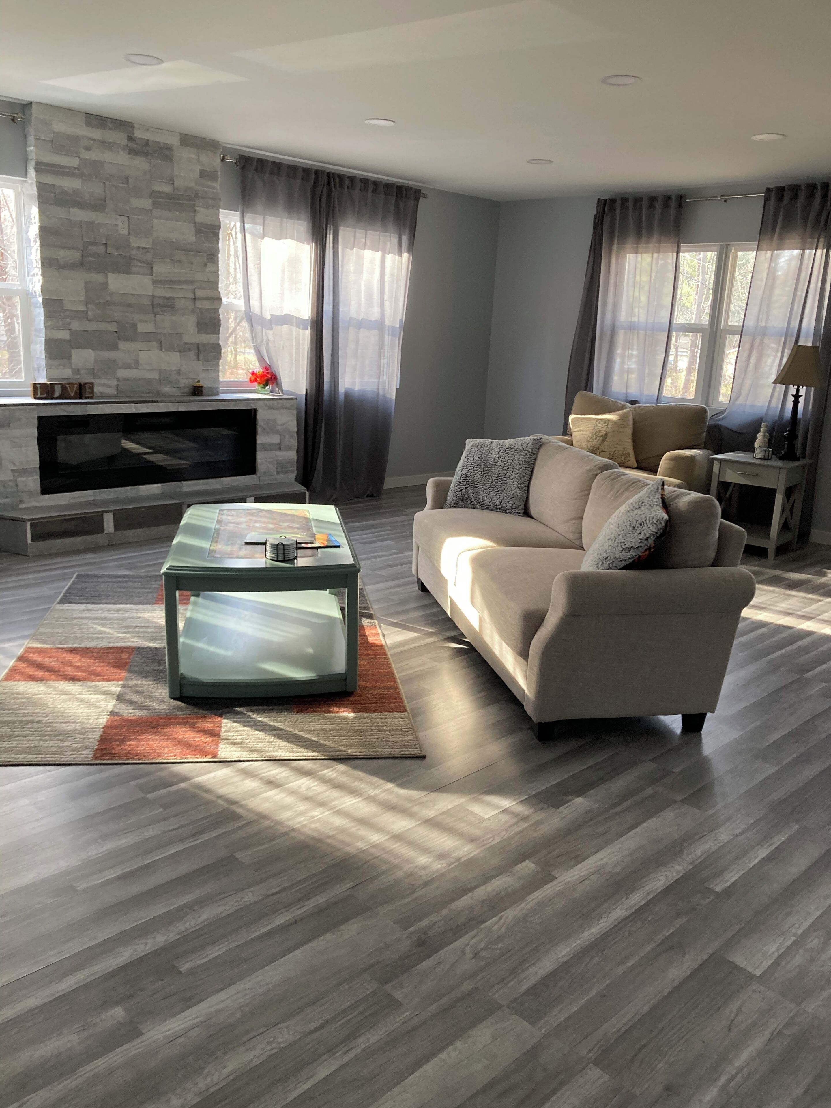 A modern living room with a stone fireplace, a beige sofa, and a glass coffee table.