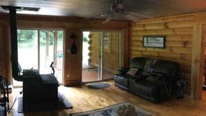 A log cabin interior with a wooden floor, a black leather sofa, a coffee table, and a ceiling fan. - 4500 sq ft Secluded Log Cabin Home on 17 acres (Waco)