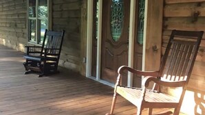 A wooden cabin with a porch, two rocking chairs, and a door with a glass panel. - 4500 sq ft Secluded Log Cabin Home on 17 acres (Waco)