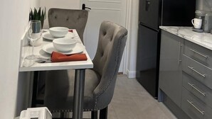 Moderni keittiö, jossa on ruokapöytä, tuolit, jääkaappi ja kahvinkeitin.