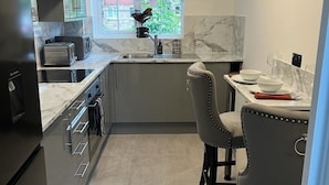 Kompakti keittiö, jossa on sisäänrakennettu uuni, pesuallas ja ruokailutila, jossa on kaksi tuolia.
