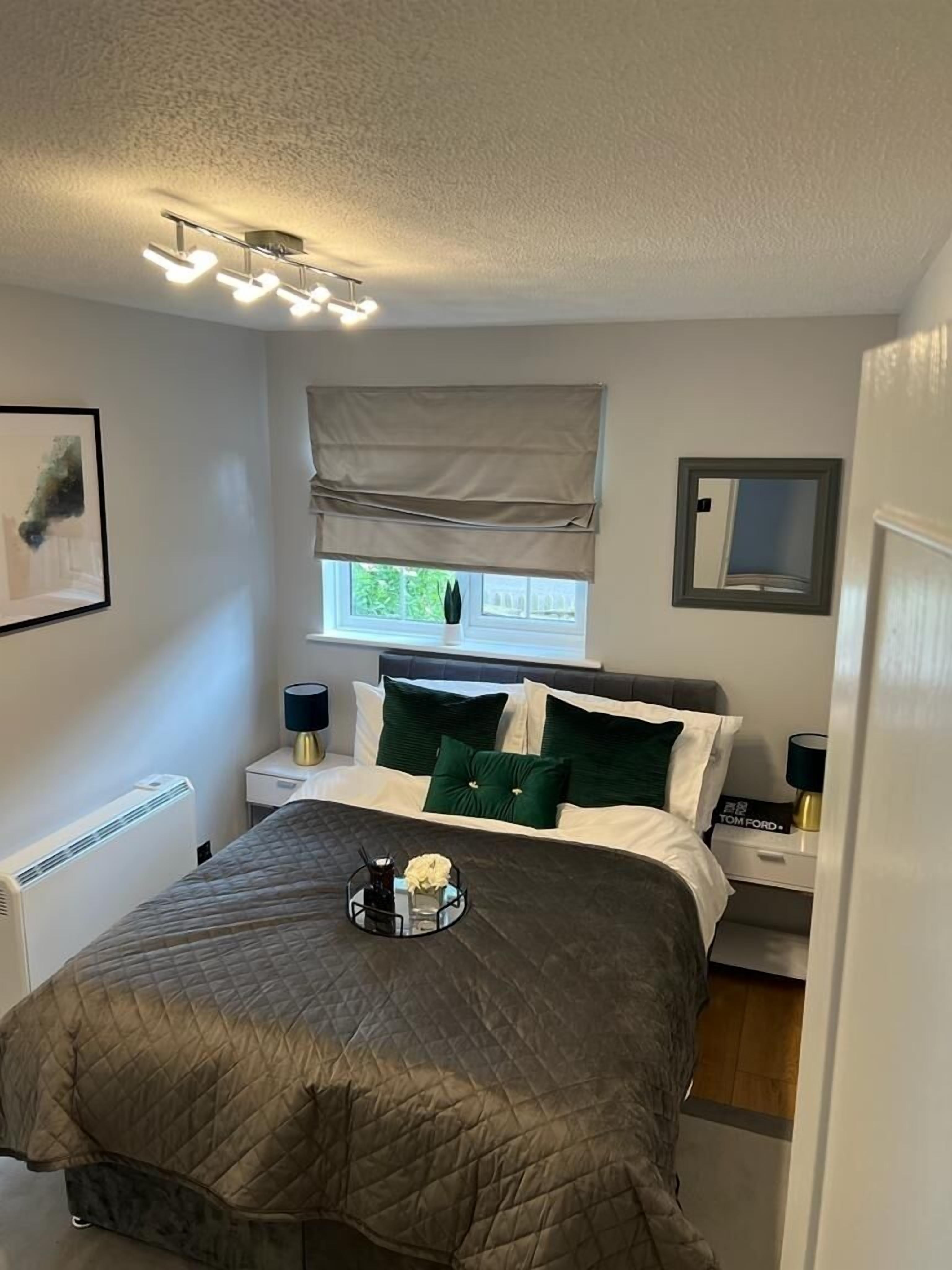 A bedroom with a bed, bedside tables, a radiator, a window with a view, and a ceiling light fixture.