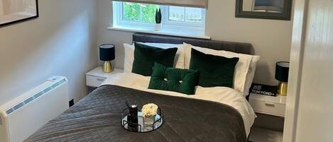 A bedroom with a bed, bedside tables, a radiator, a window with a view, and a ceiling light fixture.