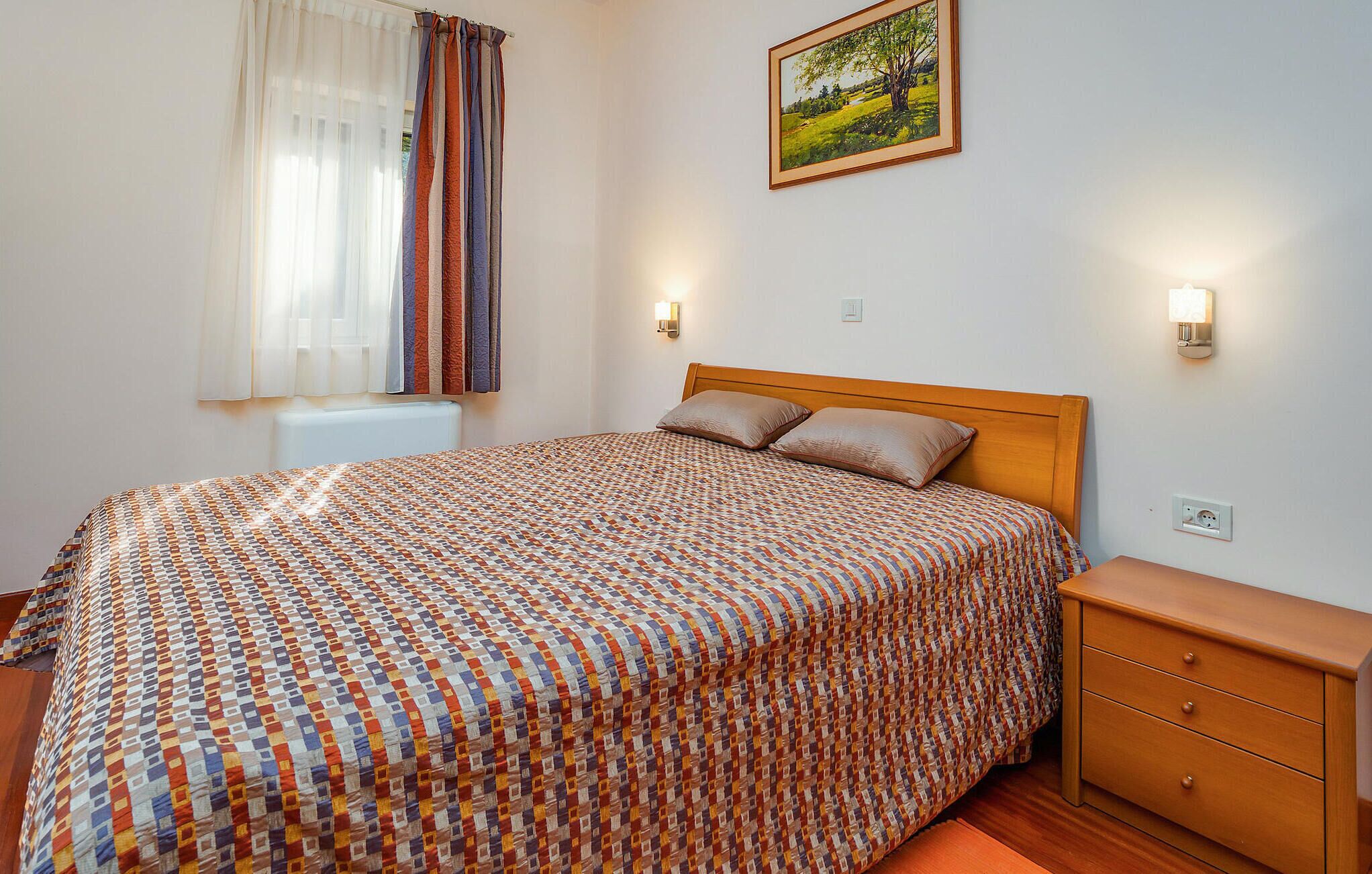 Ein Schlafzimmer mit einem gemusterten Bettbezug, einem Holzkopfschild, zwei Nachttischlampen, einem Nachttisch und einem Bild an der Wand.