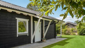 A dark wooden building with a tiled roof, white-framed windows, and a covered porch area. - Gorgeous home in Thyholm with WiFi (Thyholm)