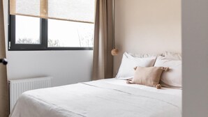 A bedroom with a bed, white bedding, a window with curtains, and a hanging light fixture. - 2 bedroom nice home in Den Oever (Den Oever)