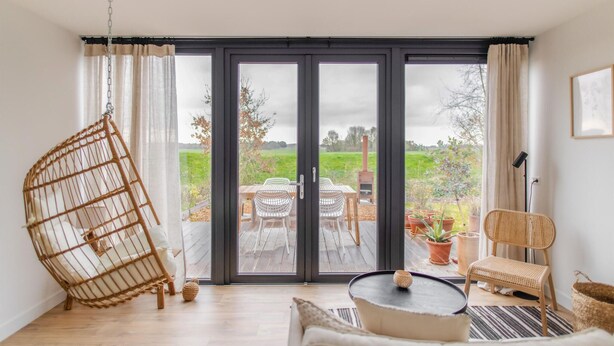 A room with a large sliding glass door leading to an outdoor patio with a table and chairs, a hanging chair, and a wicker basket. - 2 bedroom nice home in Den Oever (Den Oever)
