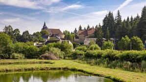 Un tranquilo pueblo a orillas del río, con casas tradicionales, un campanario de iglesia y abundante vegetación.