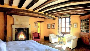 Un dormitorio con chimenea, una cama, un sillón rojo, un sofá blanco y un armario de madera.