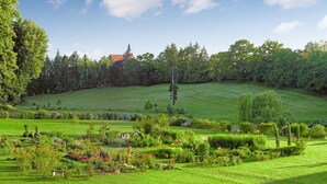 Un paisaje verde exuberante con una iglesia en una colina, jardines cuidados y diversas especies de árboles.