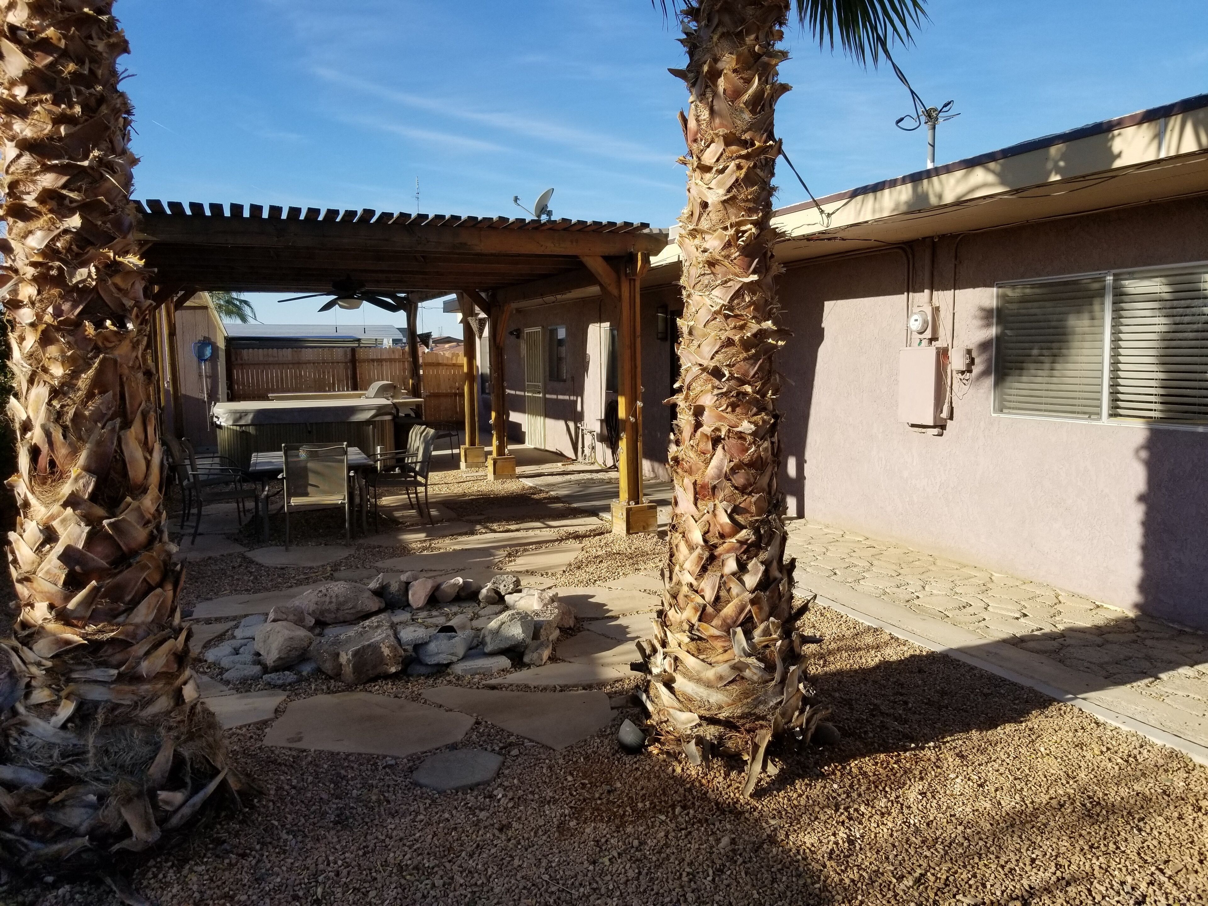 Un patio couvert avec un foyer en pierre, des meubles d’extérieur et des palmiers.