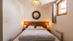 Une chambre à coucher avec une tête de lit en bois, deux lampes de chevet, un miroir rond et une fenêtre avec des rideaux.