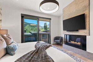 Une chambre moderne dotée d’un grand lit, d’une cheminée, d’un téléviseur fixé au mur et d’un balcon offrant une vue panoramique.