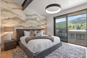 Een slaapkamer met een groot bed, een nachtkastje, een lamp en uitzicht op het landschap via een balkon, plus een plafond met een wolkentapijt.