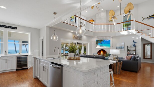 Una cocina amplia con una isla grande, armarios blancos y vistas al exterior. Una escalera conduce a un nivel superior con un balcón.