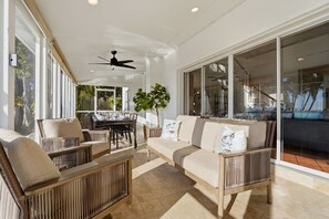 A spacious patio with a dining area, cushioned seating, and large windows offering views of the outdoors. - Luxury Bayfront Retreat w/ Guest House, Game Room & 150 Ft Waterfront (Bradenton)