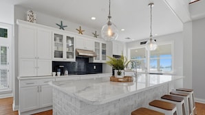 Una cocina moderna con armarios blancos, una isla grande con taburetes y estrellas de mar decorativas en la pared.