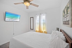 A bedroom with a bed, a ceiling fan, a TV on the wall, and a painting.