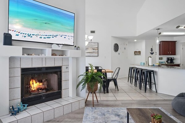 A modern living room with a fireplace, a TV mounted on the wall, and a dining area with bar stools.