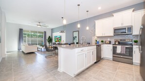 Una cocina moderna con armarios blancos, una isla grande, electrodomésticos de acero inoxidable e iluminación colgante.