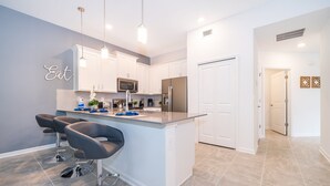 Una cocina moderna con armarios blancos, una isla central con taburetes de bar, electrodomésticos de acero inoxidable e iluminación colgante.