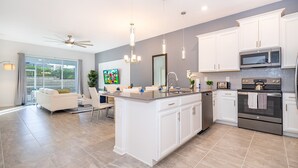 A modern kitchen with white cabinetry, a central island, stainless steel appliances, and a dining area with a white sofa and table.