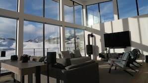 A spacious room with large windows offering a mountain view, a flat-screen TV mounted on the wall, and a cozy seating area with sofas and chairs.