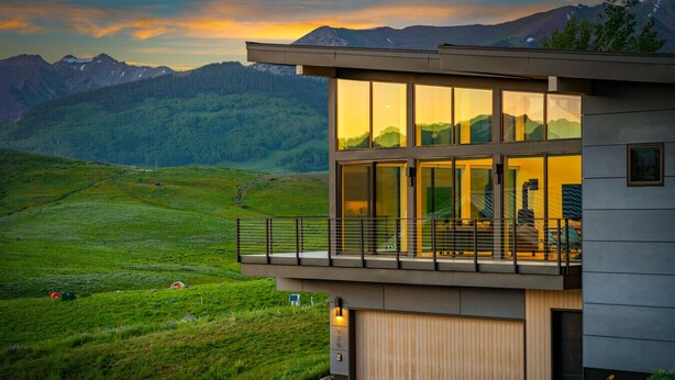 A modern two-story building with large windows, a balcony, and a view of a mountainous landscape.