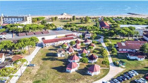 An aerial view of a coastal town with a beach, white buildings with red roofs, and a large white building with a red roof. - Beach front apartment (Cavallino-Treporti)