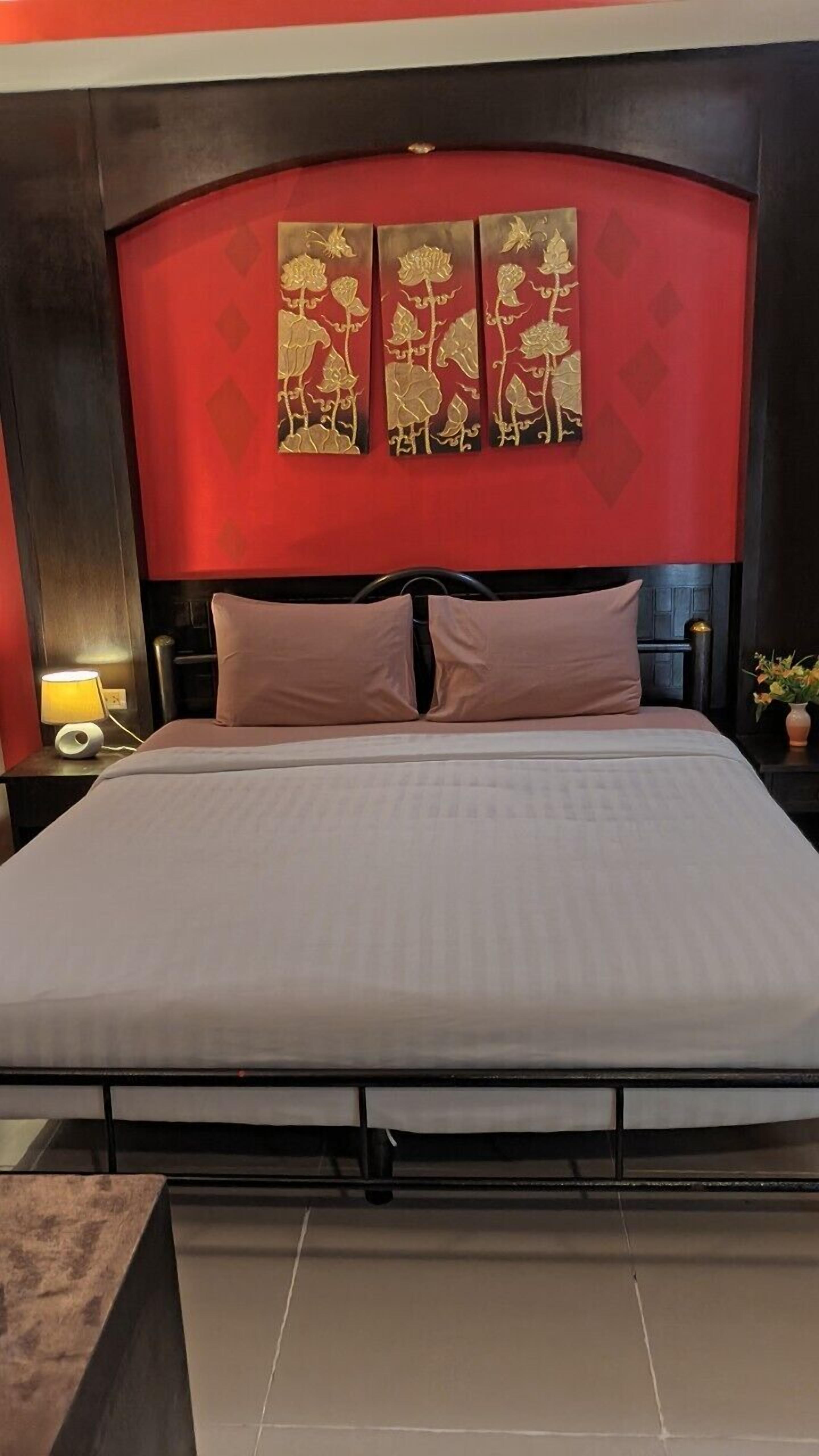 A hotel room with a large bed, a headboard with a red and black design, and three wall-mounted decorative panels.
