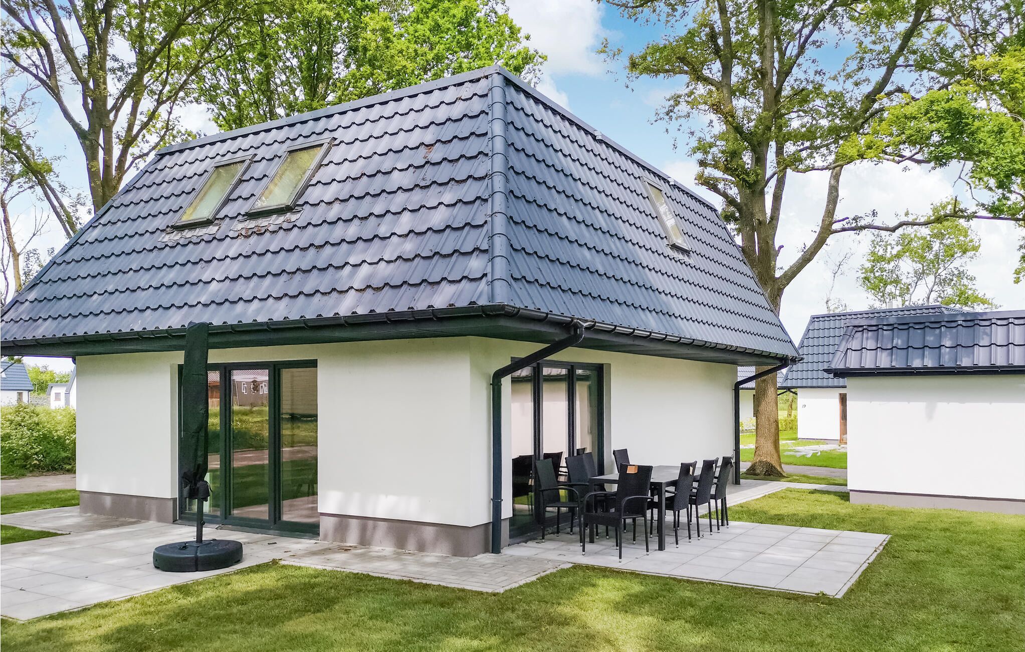 A modern house with a tiled roof, a covered patio with outdoor seating, and a well-maintained lawn.