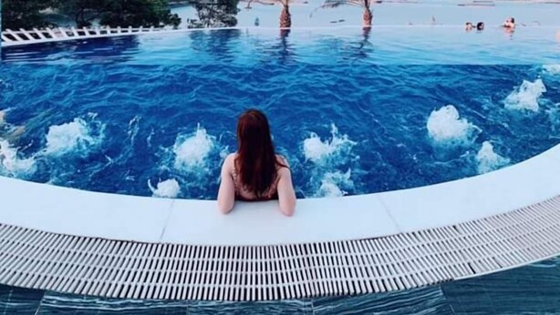 A person sitting by a pool with a view of the sea and palm trees. - BBQ Villa & Hostel Ha Long (Bai Chay)