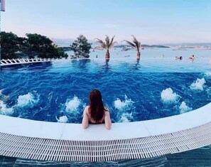A person sitting by a pool with a view of the sea and palm trees. - BBQ Villa & Hostel Ha Long (Bai Chay)