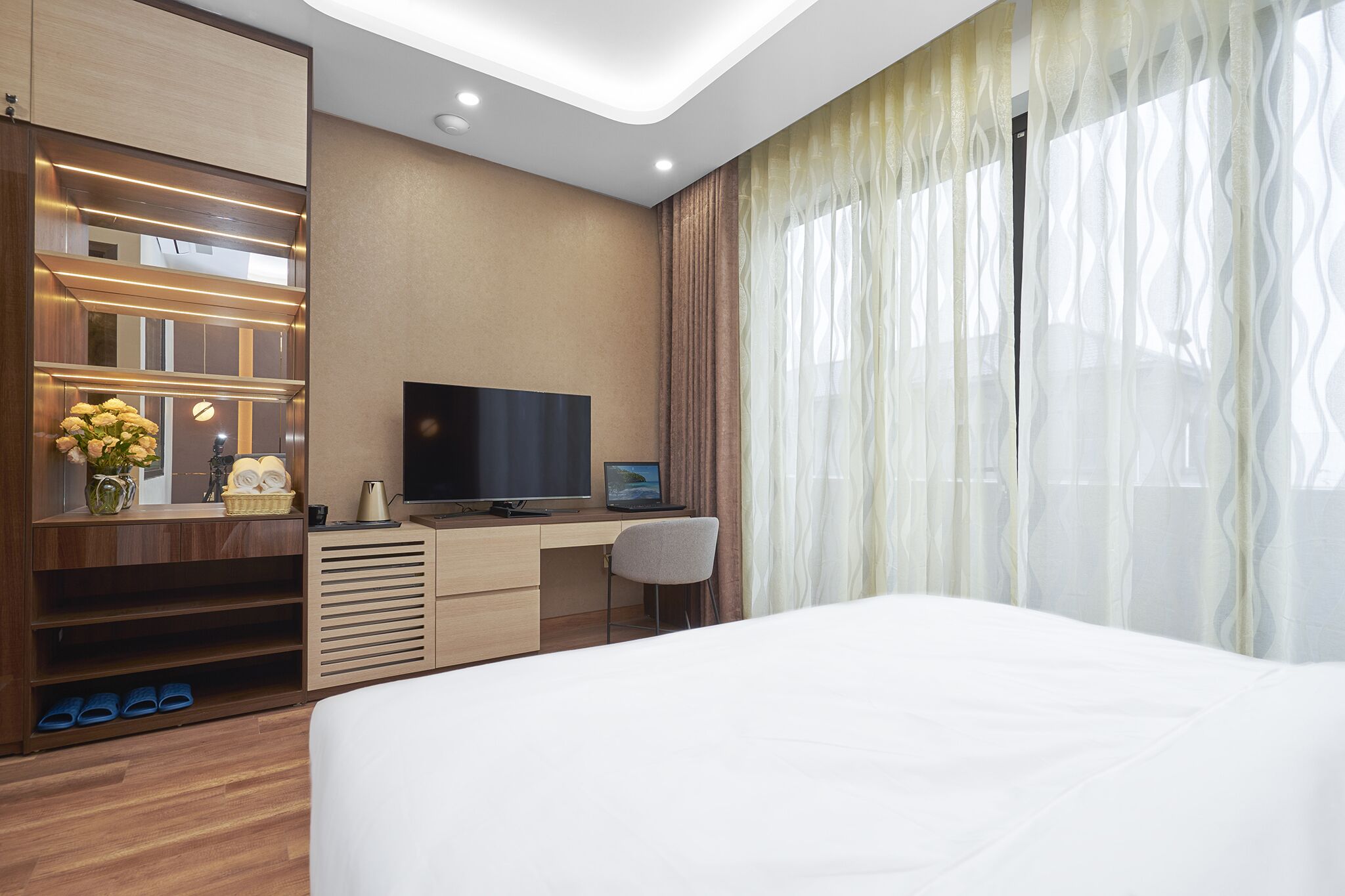 Ein modernes Hotelzimmer mit einem Bett, einem Schreibtisch mit Flachbildfernseher, einem Laptop und einer kleinen Sitzecke.