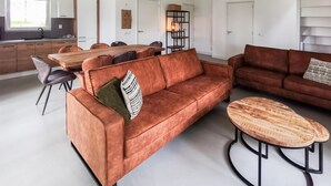 En moderne stue med en brun sofa, et træbord som sofabord og et spiseområde med et træbord og stole.