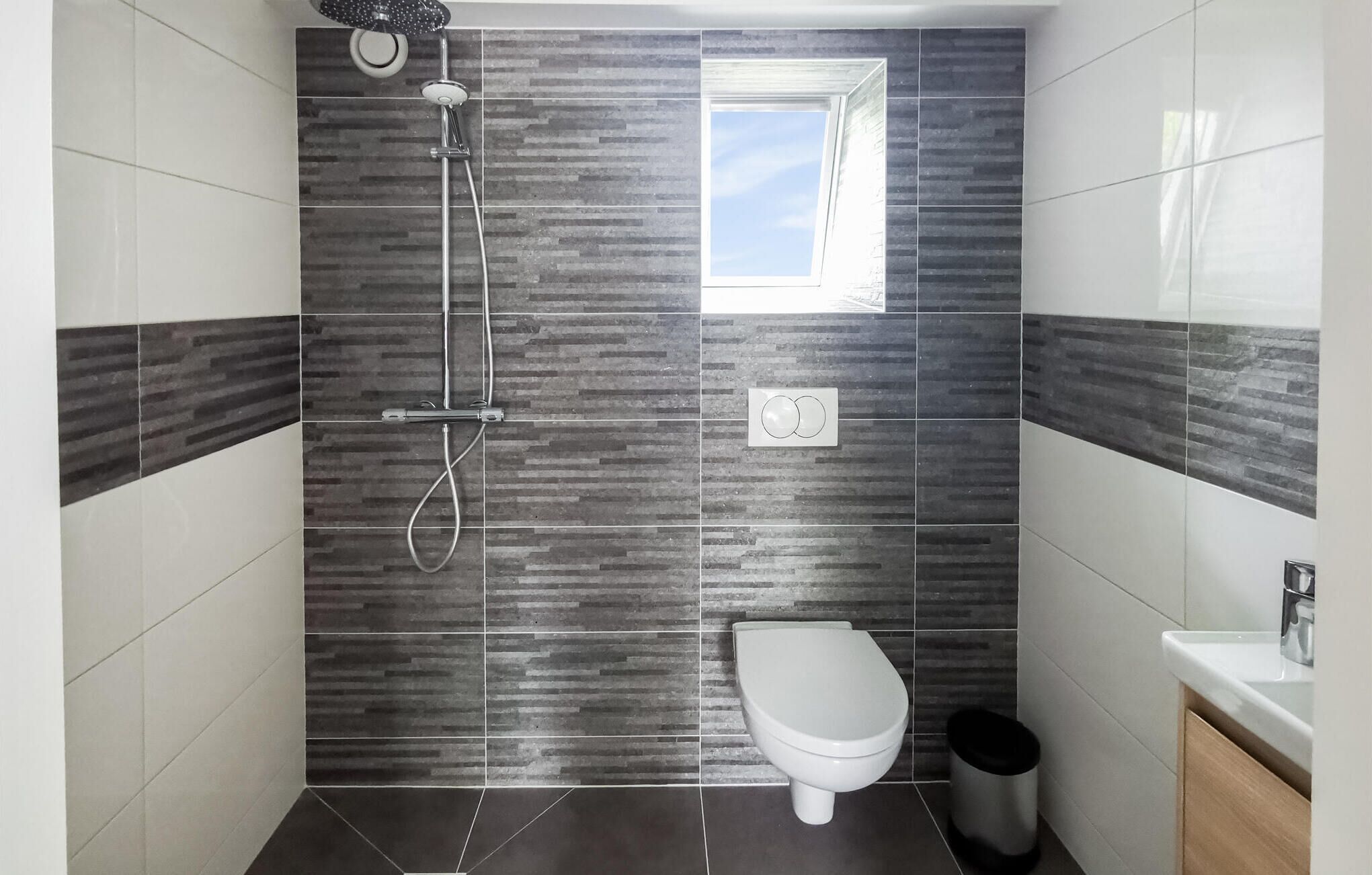 A bathroom with a shower, toilet, and a window.